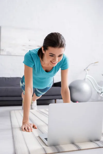 Joyeuse femme enceinte en vêtements de sport faisant de l'exercice près d'un ordinateur portable dans le salon — Photo de stock