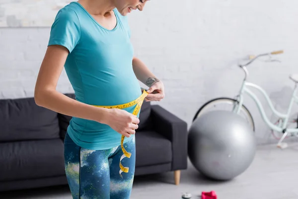 Happy pregnant sportswoman measuring belly at home — Stock Photo