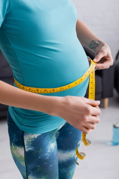 Ausgeschnittener Blick auf tätowierte schwangere Sportlerin, die ihren Bauch zu Hause misst — Stockfoto