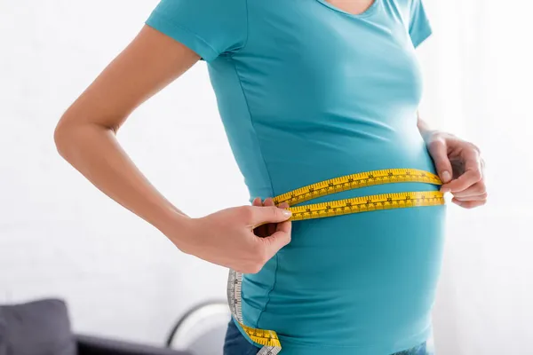 Vista recortada de la deportista embarazada que mide el vientre en casa - foto de stock