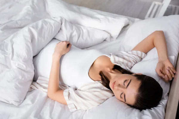 High angle view of pregnant young woman in pajamas sleeping in bed — Stock Photo