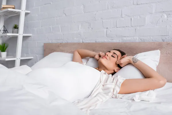 Tattooed and pleased woman with closed eyes lying in bed — Stock Photo