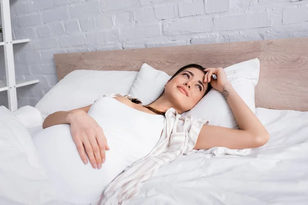 Awake pregnant woman with tattoo lying in bed — Stock Photo