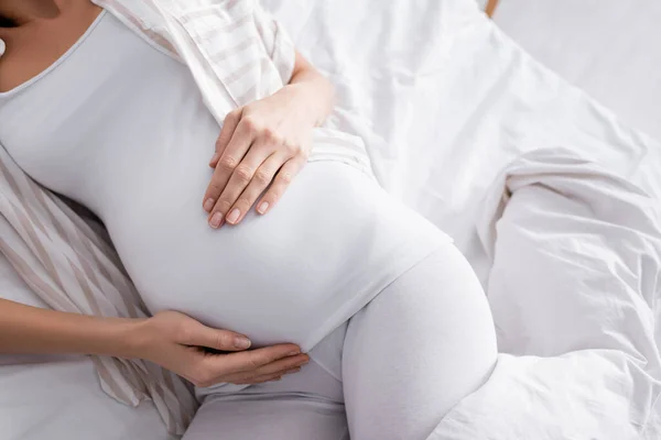 Vista superior da mulher grávida tocando barriga enquanto deitado na cama — Fotografia de Stock