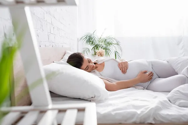 Jeune femme enceinte toucher le ventre tout en étant couché dans la chambre — Photo de stock