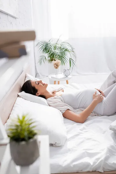 Vista lateral da jovem grávida feliz tocando barriga enquanto deitado no quarto — Fotografia de Stock