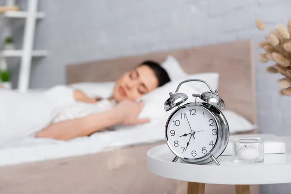 Despertador retro en mesa de centro cerca de mujer dormida borrosa - foto de stock