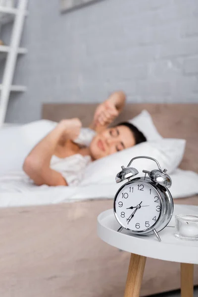 Retro despertador na mesa de café perto mulher sonolenta borrada — Fotografia de Stock