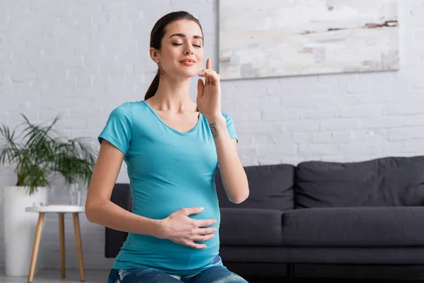 Tätowierte Schwangere mit geschlossenen Augen meditiert im Wohnzimmer — Stockfoto