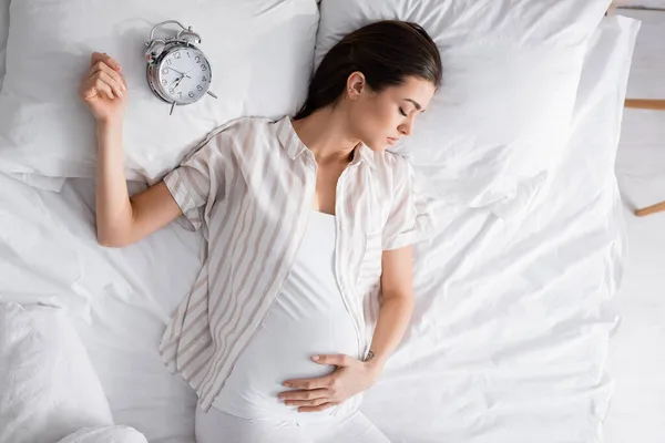 Ansicht von oben: Schwangere schläft in der Nähe des Weckers auf Kopfkissen — Stockfoto