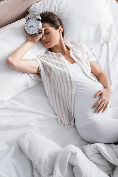 Vue grand angle de la femme enceinte dormant avec réveil — Photo de stock