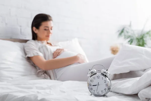 Despertador retro na cama perto de mulher grávida borrada — Fotografia de Stock