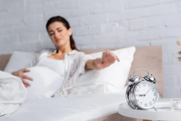Retro alarm clock on coffee table near blurred pregnant woman in bed — Stock Photo