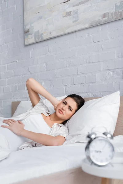 Displeased pregnant woman looking at blurred alarm clock — Stock Photo