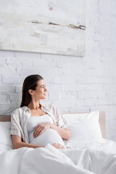Mujer embarazada feliz mirando hacia otro lado en el dormitorio - foto de stock