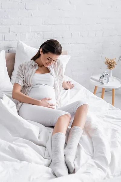 Mulher grávida positiva olhando para a barriga no quarto — Fotografia de Stock