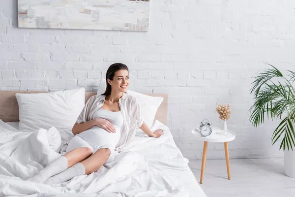 Mujer embarazada sonriente mirando hacia otro lado en el dormitorio - foto de stock