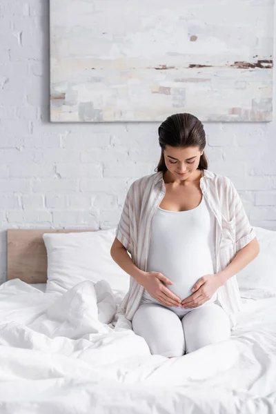 Mulher grávida positiva olhando para a barriga no quarto — Fotografia de Stock