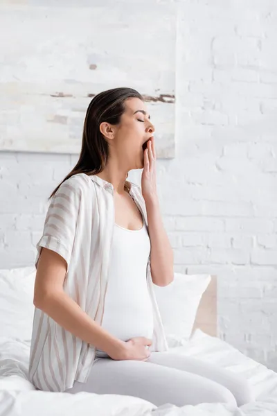 Sleepy pregnant woman yawning and covering mouth in bedroom — Stock Photo