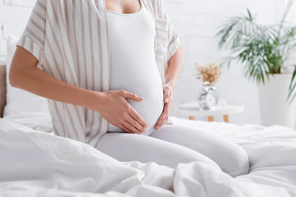 Teilansicht einer tätowierten Schwangeren, die ihren Bauch im Schlafzimmer berührt — Stockfoto