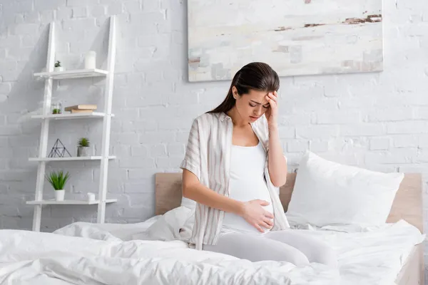 Erschöpfte Schwangere blickt auf Bauch im Schlafzimmer — Stockfoto