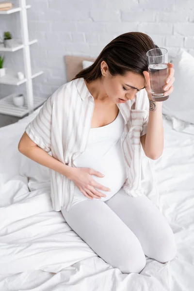 Giovane donna incinta che tiene un bicchiere d'acqua mentre sente dolore addominale — Foto stock