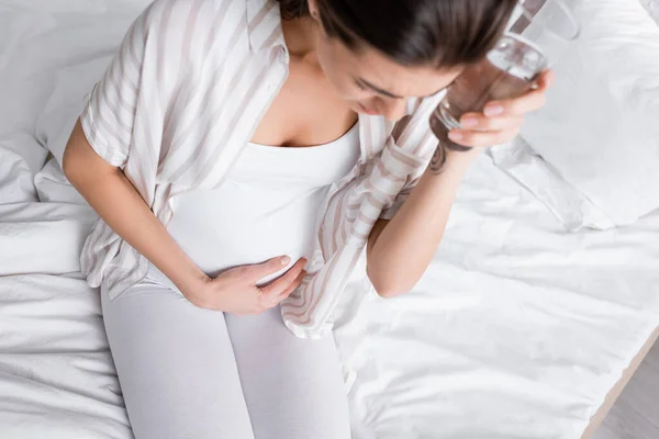 Pregnant woman holding glass of water while feeling abdomen pain — Stock Photo