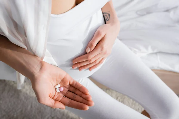 Vista recortada de mujer embarazada tatuada sosteniendo píldoras - foto de stock