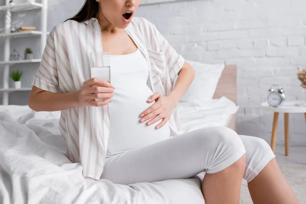 Vue partielle de la femme enceinte se sentant crampe tout en tenant un verre d'eau — Photo de stock