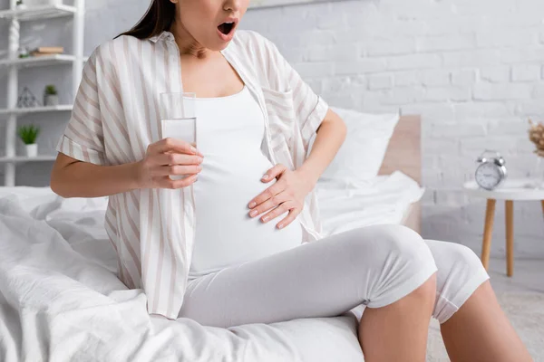 Partial view of pregnant woman feeling cramp while holding glass of water — Stock Photo