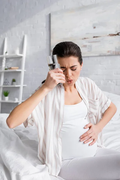 Giovane donna incinta sensazione di crampo e tenendo un bicchiere d'acqua — Foto stock