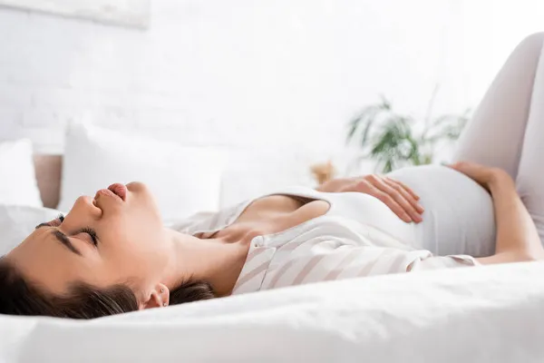 Young pregnant woman feeling cramp while lying on bed — Stock Photo