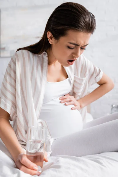 Беременная женщина чувствует спазм, держа стакан воды — стоковое фото