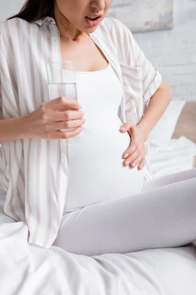 Обрізаний вид вагітної жінки, що відчуває судоми, тримаючи склянку води — стокове фото