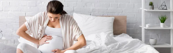 Young pregnant woman suffering from cramp while sitting on bed, banner — Stock Photo