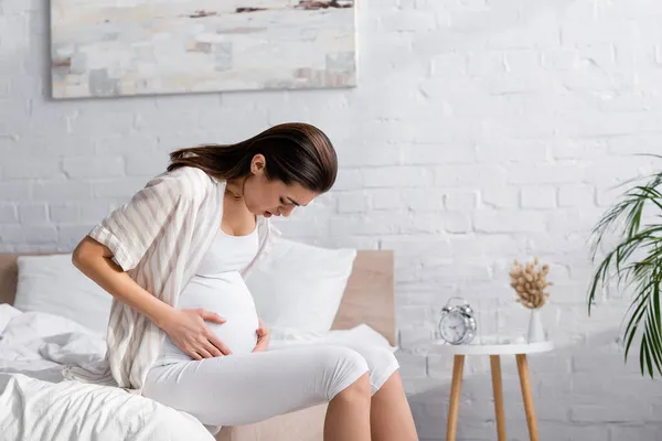 Mujer embarazada con los ojos cerrados que sufren de calambres en el dormitorio - foto de stock
