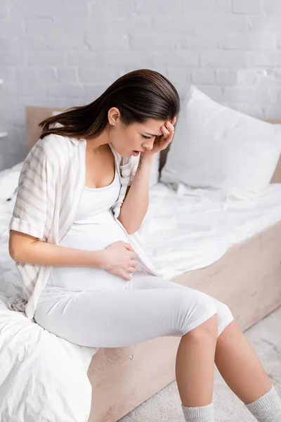 Mujer embarazada que sufre de calambres en el dormitorio - foto de stock
