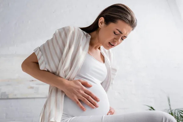 Young pregnant woman with closed eyes feeling abdominal pain — Stock Photo