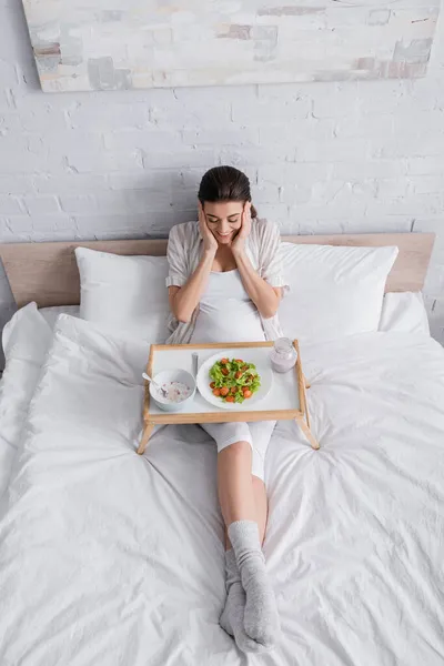 Vista ad alto angolo di eccitata donna incinta guardando vassoio con pasto — Foto stock