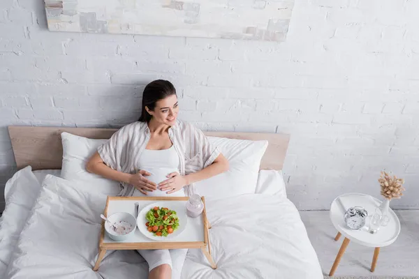 Visão de alto ângulo da mulher grávida feliz sentada perto da refeição na bandeja — Fotografia de Stock