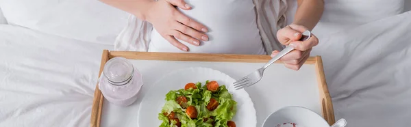 Vista recortada de la mujer embarazada sosteniendo tenedor cerca de la comida en bandeja, pancarta - foto de stock