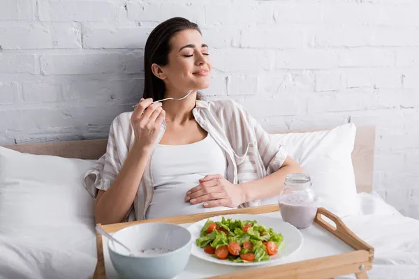 Cheerful pregnant woman holding fork near tasty meal on tray — Stock Photo