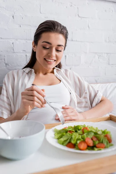 Весела вагітна жінка тримає виделку біля смачної їжі на лотку — стокове фото