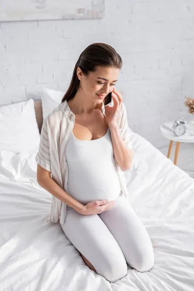 Glückliche Schwangere spricht im Schlafzimmer auf Smartphone — Stockfoto