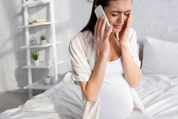 Mujer embarazada triste hablando en el teléfono inteligente en el dormitorio - foto de stock