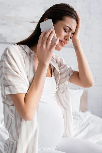 Расстроена беременная женщина разговаривает на смартфоне в спальне — стоковое фото