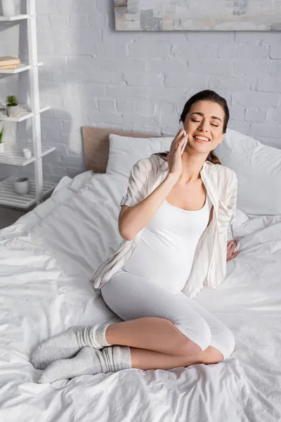 Gioiosa donna incinta che parla su smartphone in camera da letto — Foto stock