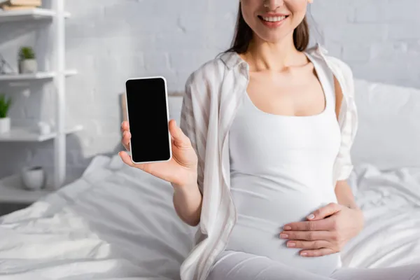 Vista recortada de la mujer embarazada feliz sosteniendo teléfono inteligente con pantalla en blanco - foto de stock