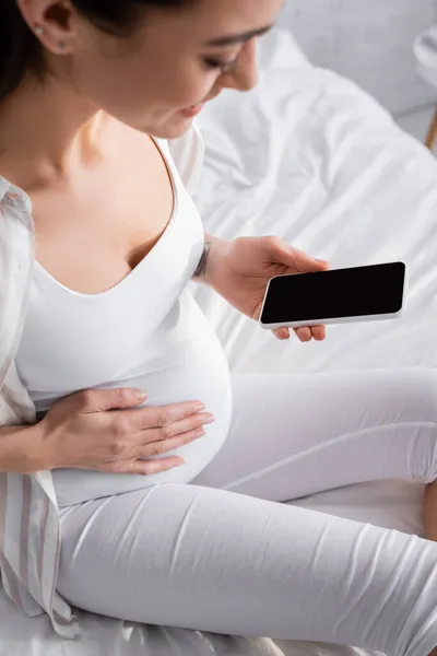 Mulher grávida turva e feliz segurando smartphone com tela em branco — Fotografia de Stock