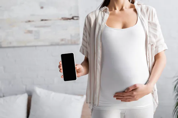 Partial view of young pregnant woman holding smartphone with blank screen — Stock Photo